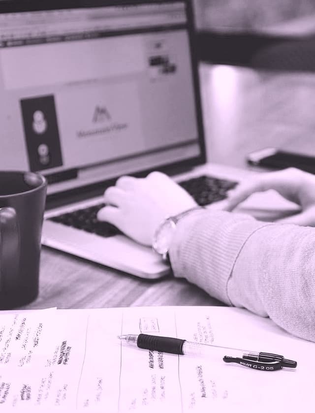 Image of a woman working at a laptop with her notebook, pen, and mug visible